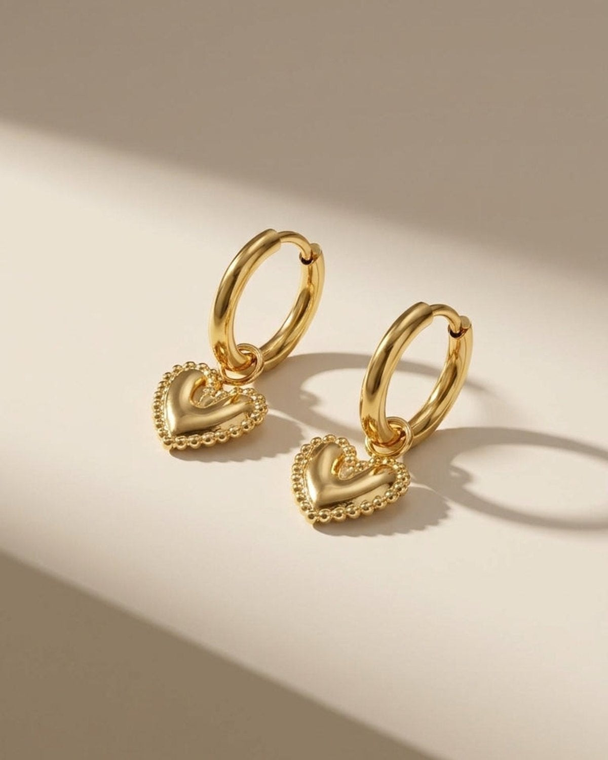 Gold hoop earrings with puffy heart pendants featuring beaded borders, presented on a light background.