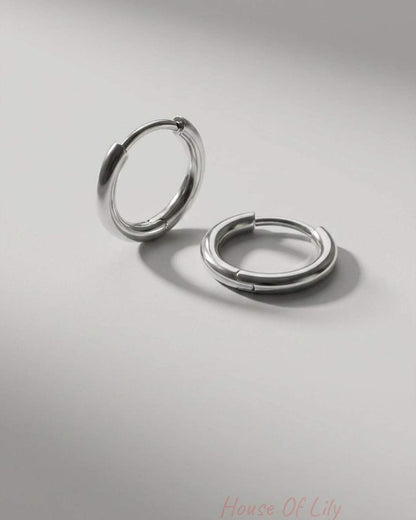 Minimalist silver huggie hoop earrings with a smooth, polished finish on a light grey background.