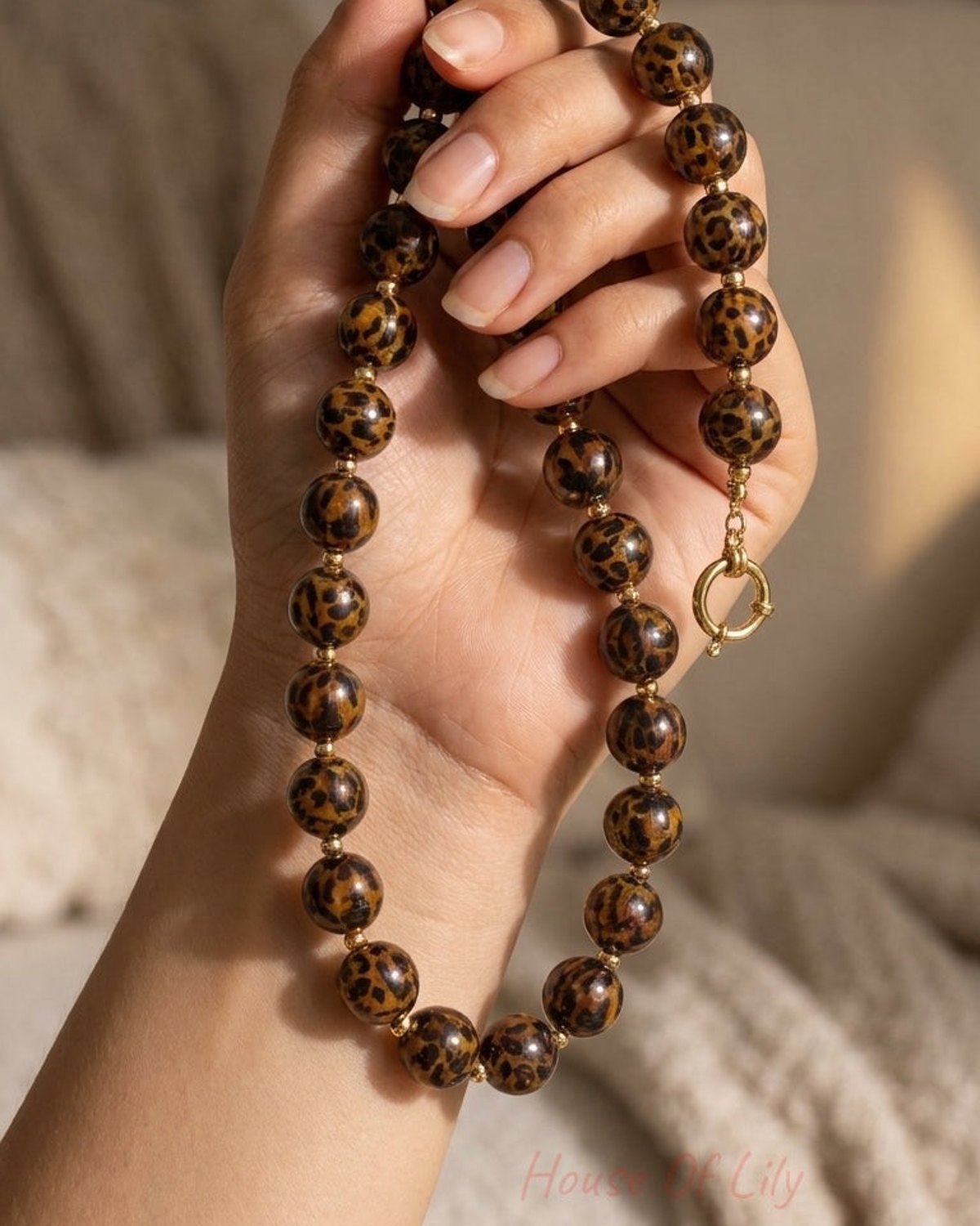 Hand holding a beaded necklace featuring round brown beads with black leopard print spots and gold spacer beads.
