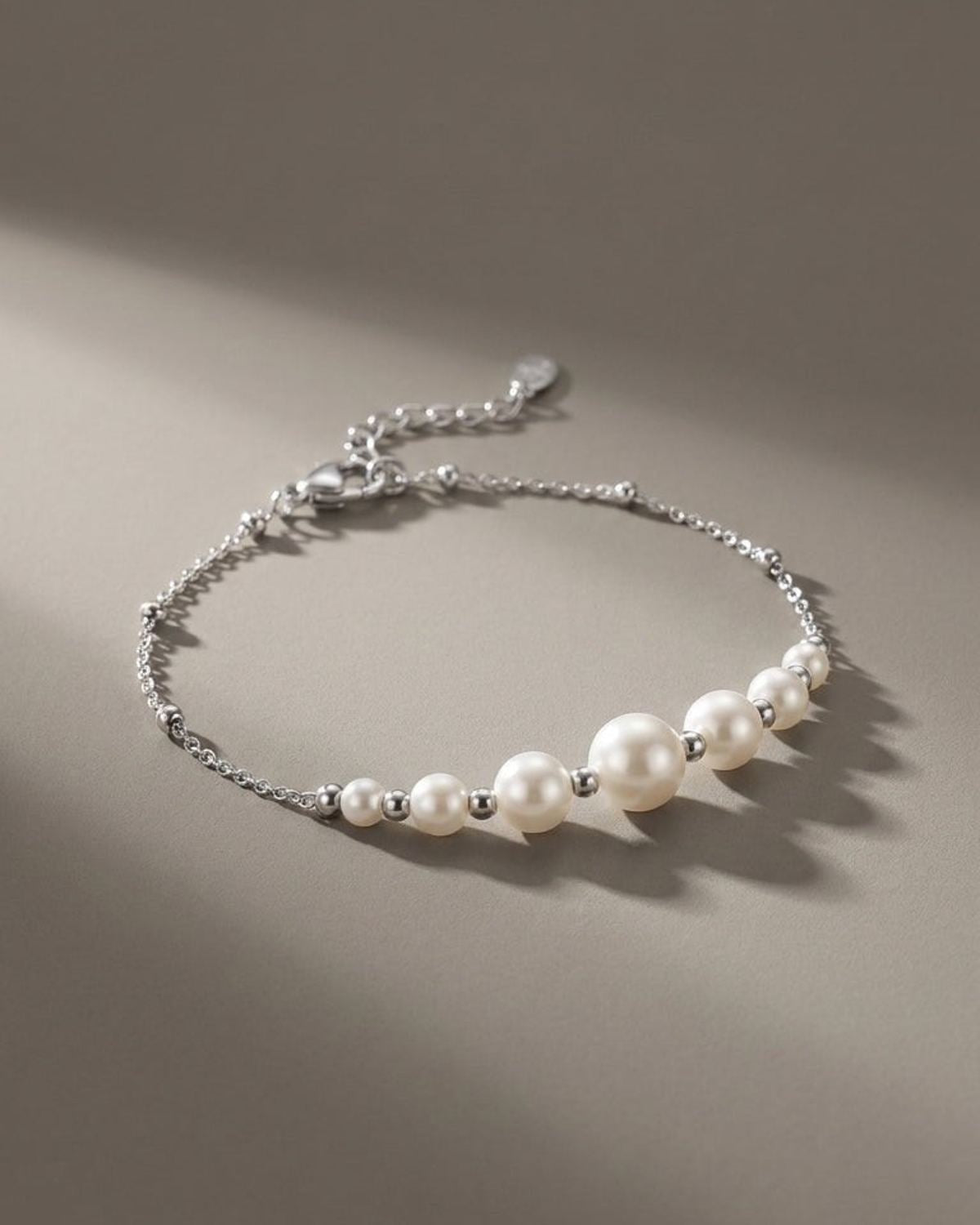 A silver-tone chain bracelet features graduated white pearls, separated by small metal beads, on a gray surface.