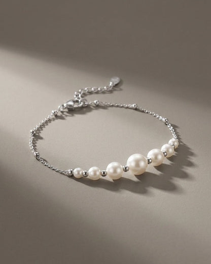 A silver-tone chain bracelet features graduated white pearls, separated by small metal beads, on a gray surface.