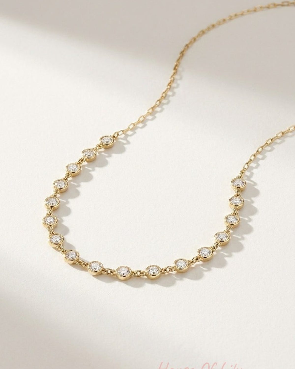 A gold chain necklace featuring a curved row of bezel-set round crystals displayed on a white surface.