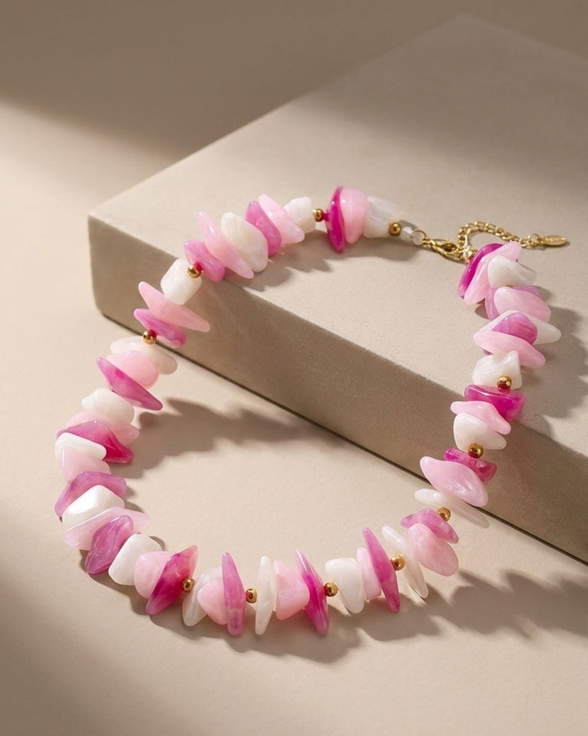 A necklace featuring irregular tumbled stone beads in shades of pink, white, and magenta, separated by small gold beads.