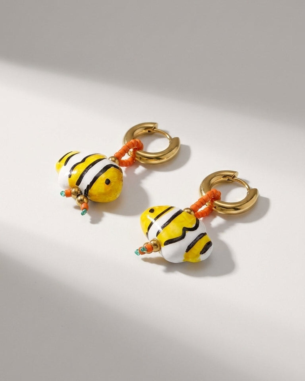 Gold hoop earrings featuring yellow, white, and black striped fish-shaped glass beads with orange seed beads.