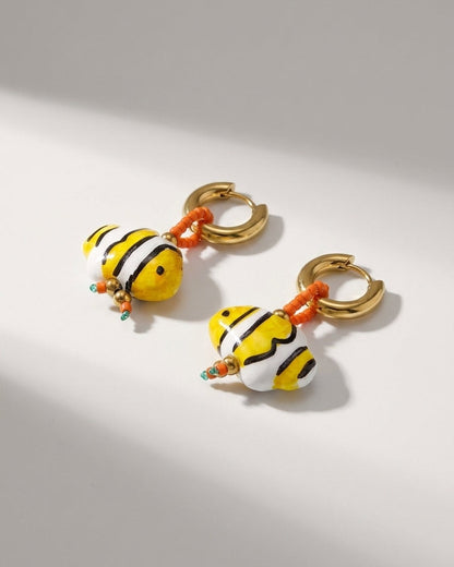 Gold hoop earrings featuring yellow, white, and black striped fish-shaped glass beads with orange seed beads.