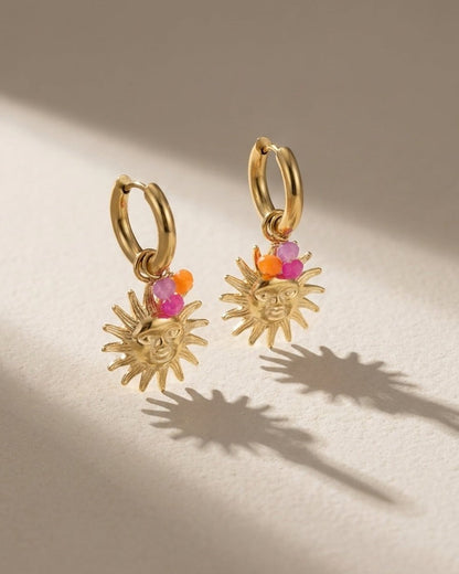 Gold hoop earrings with dangling sun face charms, accented by small pink and orange bead clusters.