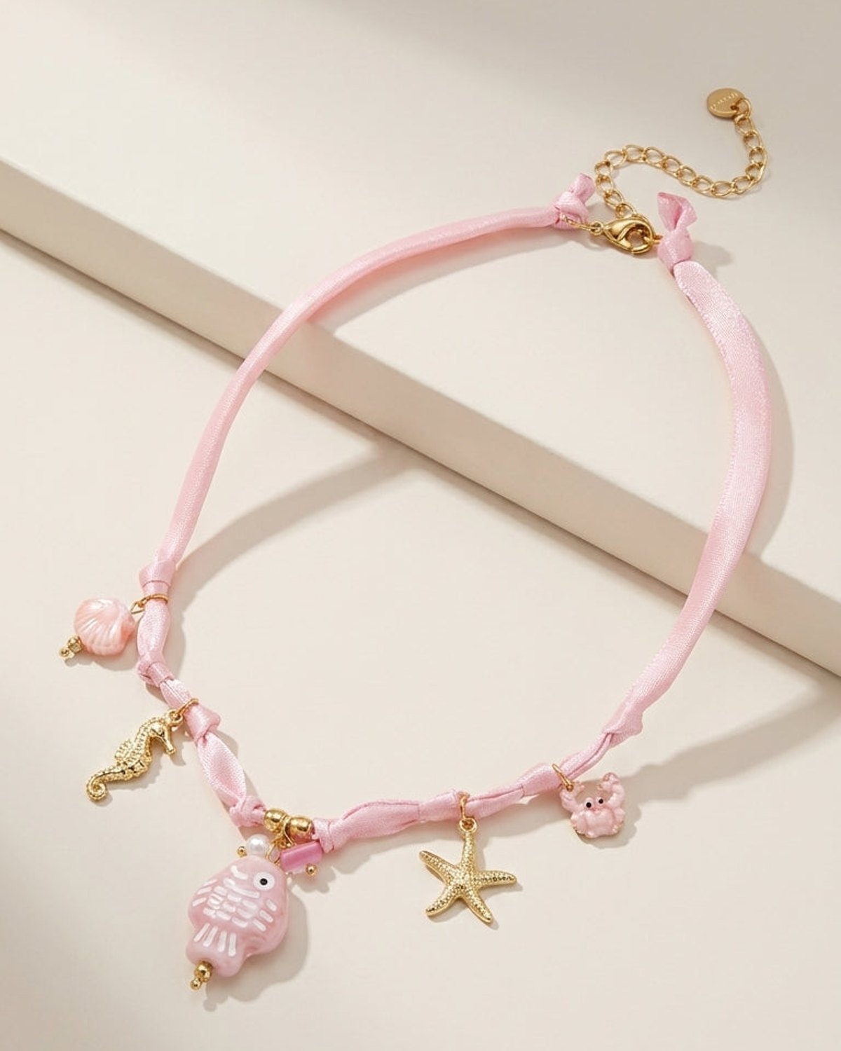 Pink ribbon necklace with gold ocean charms, including a fish, seahorse, starfish, crab, and shell.