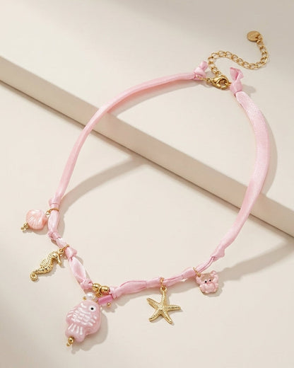 Pink ribbon necklace with gold ocean charms, including a fish, seahorse, starfish, crab, and shell.