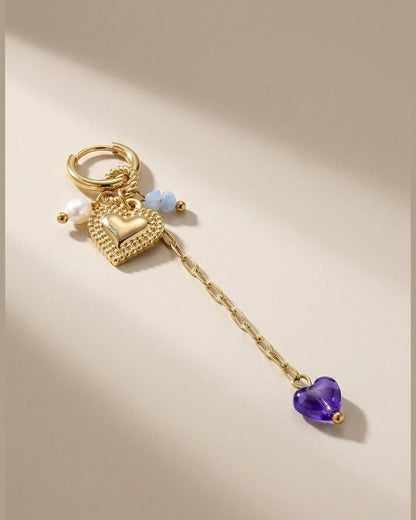 Gold hoop earring with a textured heart charm, pearl and blue beads, and a dangling chain with a purple heart.