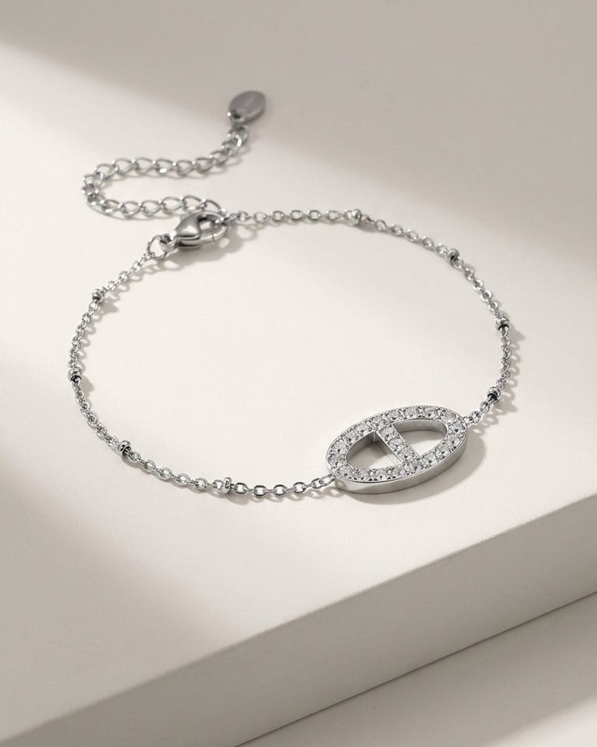 A silver chain bracelet featuring a paved oval link center rests on a white surface.