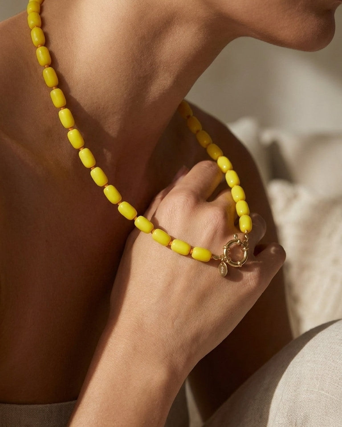 A person wearing a short necklace of chunky, oblong yellow beads with a gold clasp.