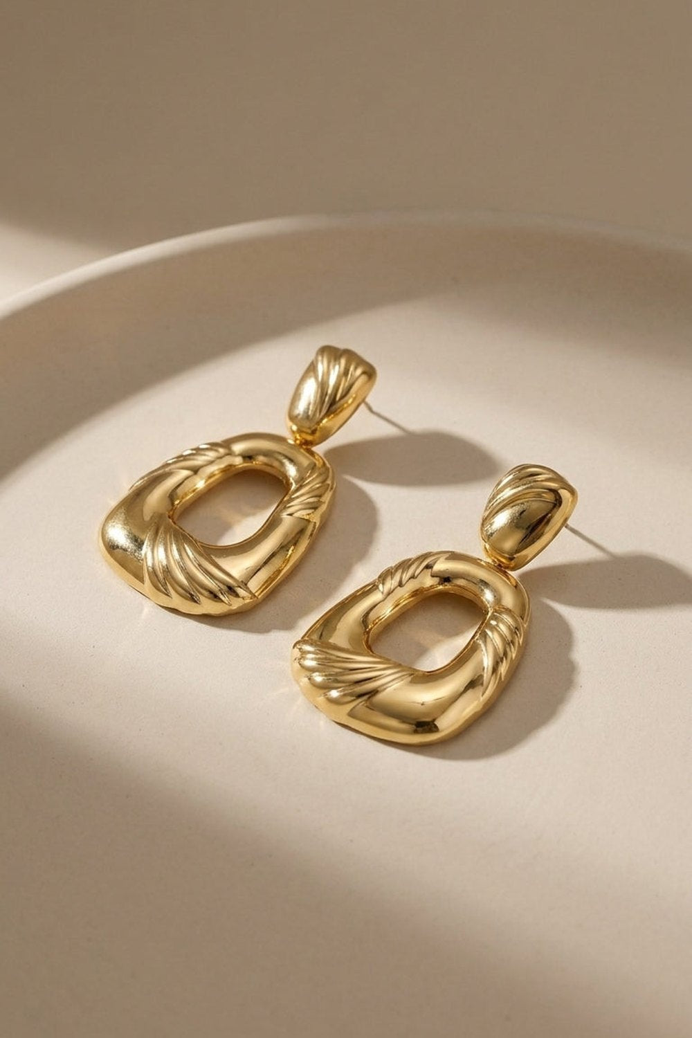 Gold geometric drop earrings with sculpted, fluted detailing on the open-center links and posts.