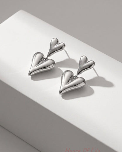 Polished silver drop earrings featuring two connected puffed heart charms on a white display block.