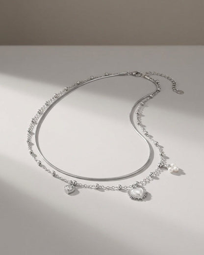 Silver layered coquette necklace with heart charms and pearl accents on a light surface.