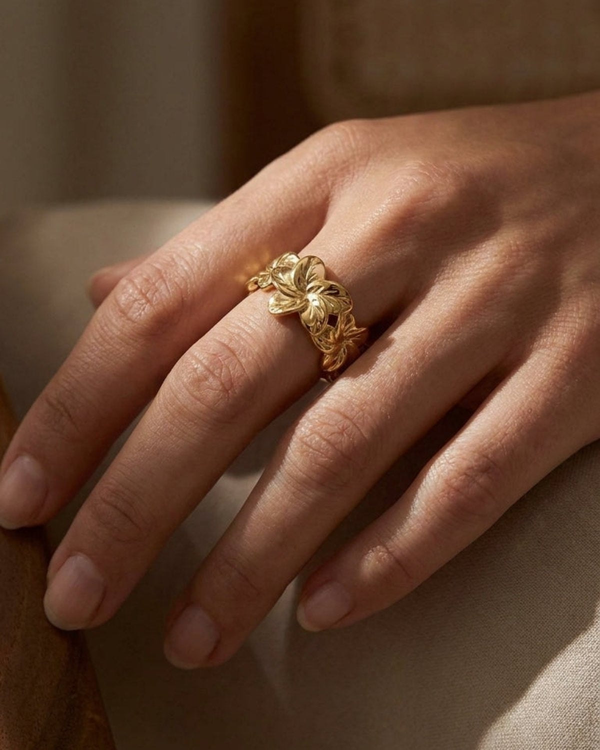 Polished gold band ring featuring a carved floral hibiscus bloom pattern worn on a finger.
