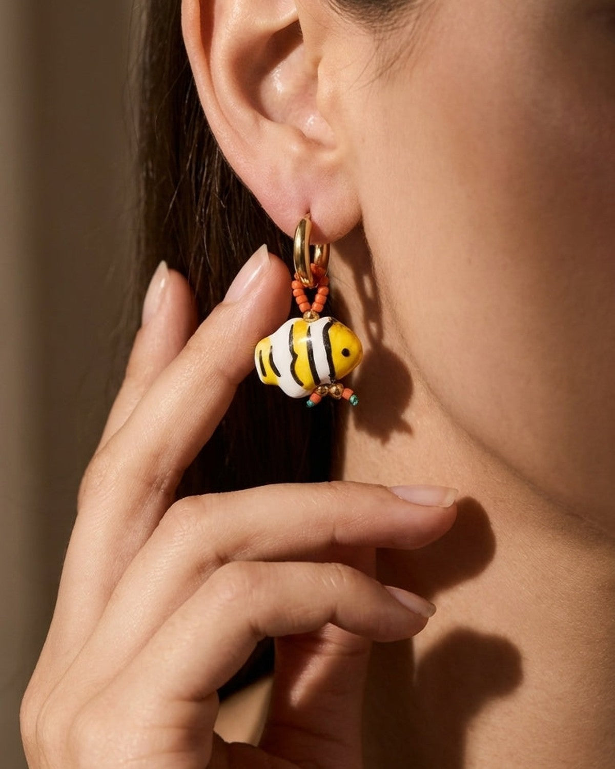 Gold hoop earrings with a glass fish bead, painted yellow, white, and black with striped patterns.