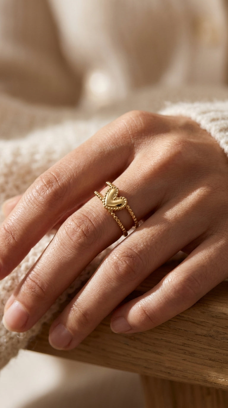 Gold Double Trouble ring featuring a heart charm on a double-band beaded design, worn on a finger.