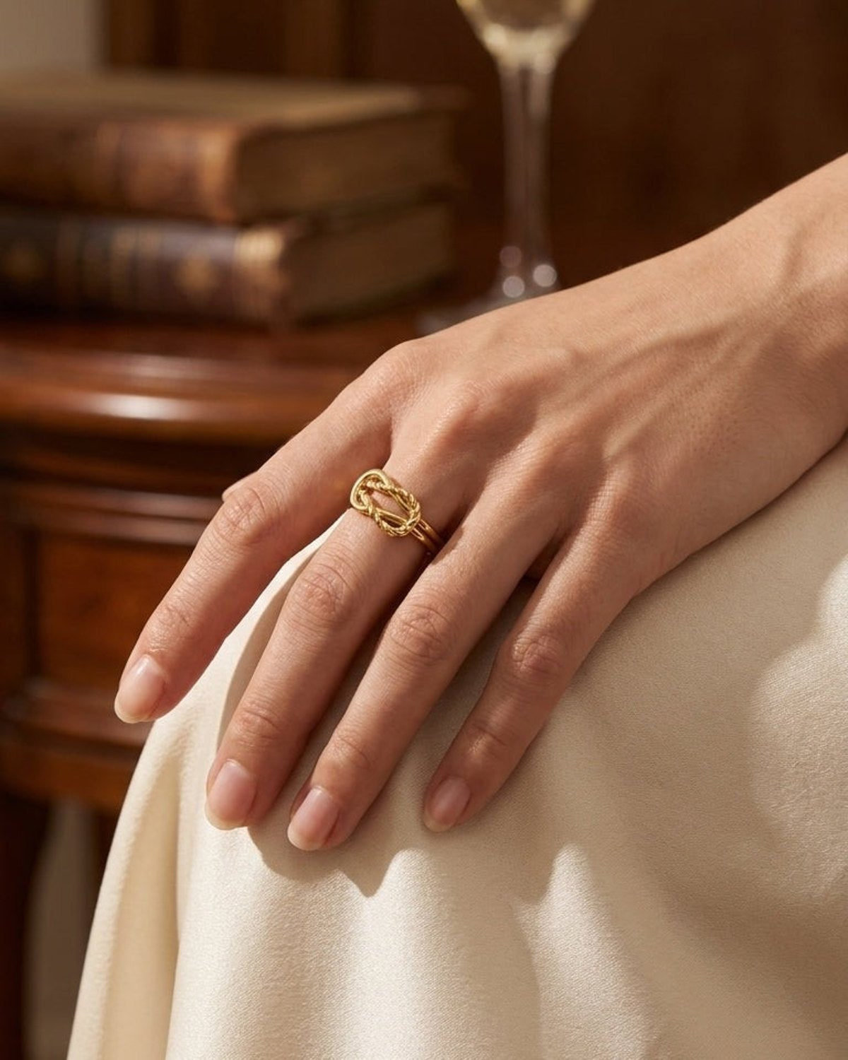 A woman's hand wears a polished gold twisted knot statement ring on her ring finger.
