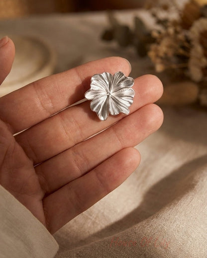 A silver flower-shaped earring rests in the palm of an open hand.