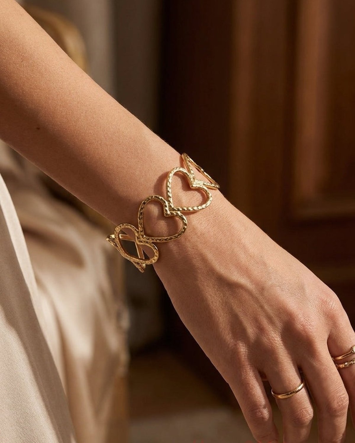 Gold-colored cuff bracelet featuring a row of connected open-work hearts with a textured finish worn on a wrist.