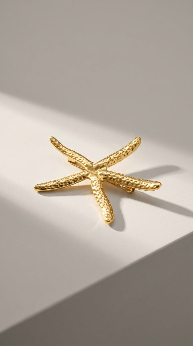 Gold-toned starfish brooch with a textured, hammered metal finish on a light, neutral background.