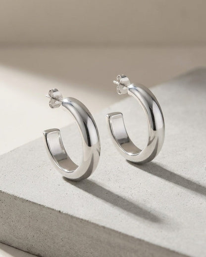 Minimalist silver hoop earrings with a thick, polished, chunky design on a grey stone surface.
