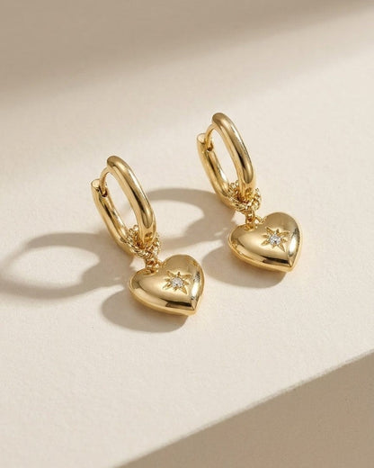 Gold-plated huggie hoop earrings with dangling puffy hearts featuring a central star-set zircon stone.