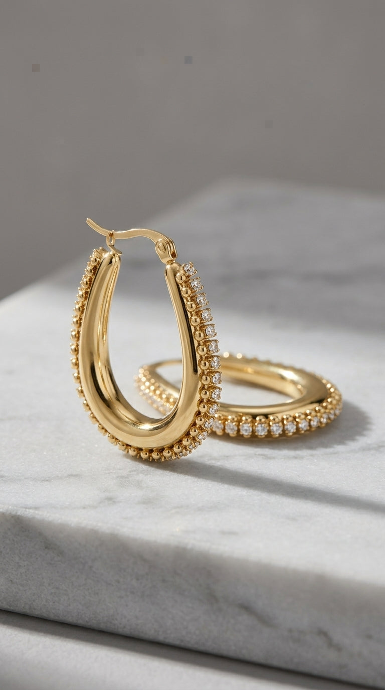 Drip Drop Glow gold hoop earrings featuring a beaded edge and a row of sparkling pavé stones on a marble surface.