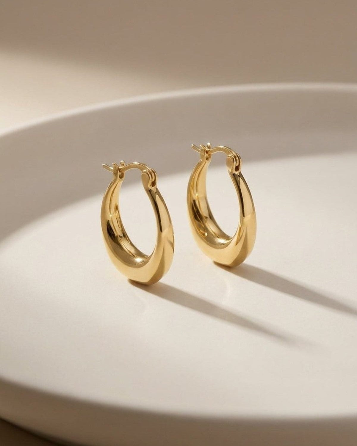 A pair of thick, polished gold hoop earrings with an asymmetrical, melted-curve design and hinged closures.