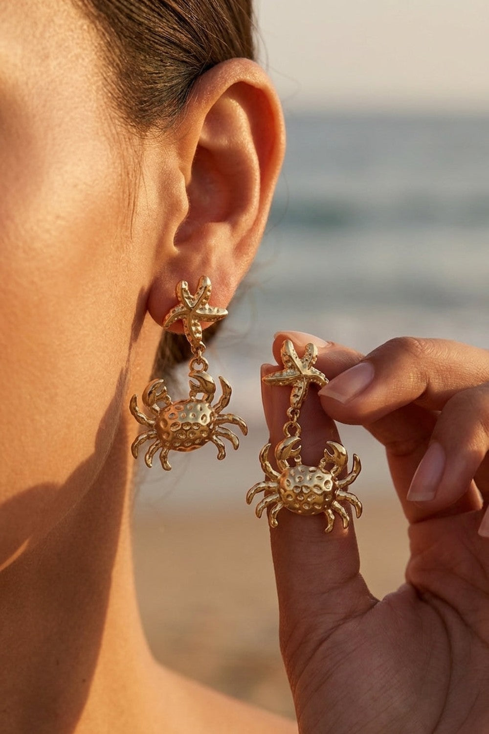 Gold drop earrings featuring a starfish stud connected to a textured crab pendant.
