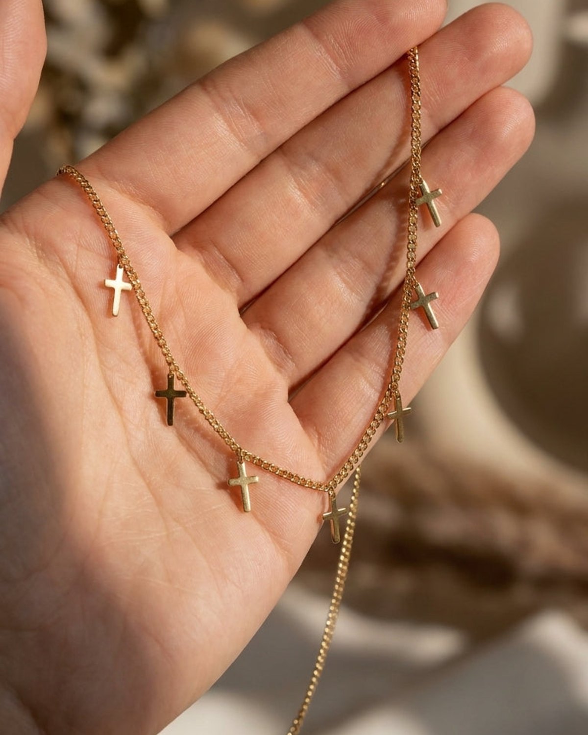 Gold curb chain necklace with multiple small cross charms resting in an open palm.