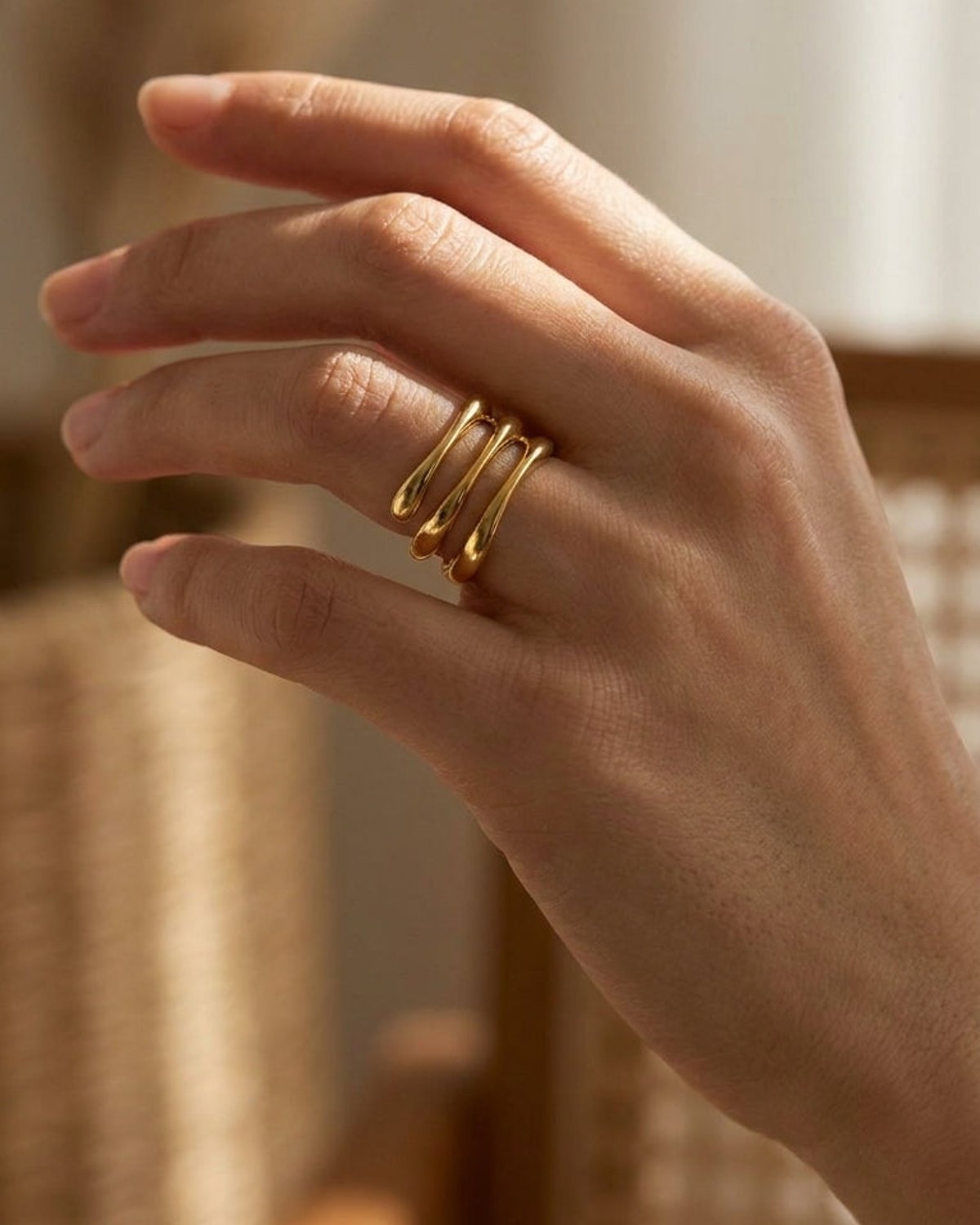 Gold-finished Wave Stack Ring with three curved, polished bands worn on a finger.