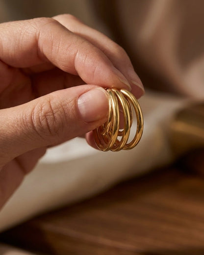 A hand holds up a cluster of four polished gold hoop earrings against a neutral background.