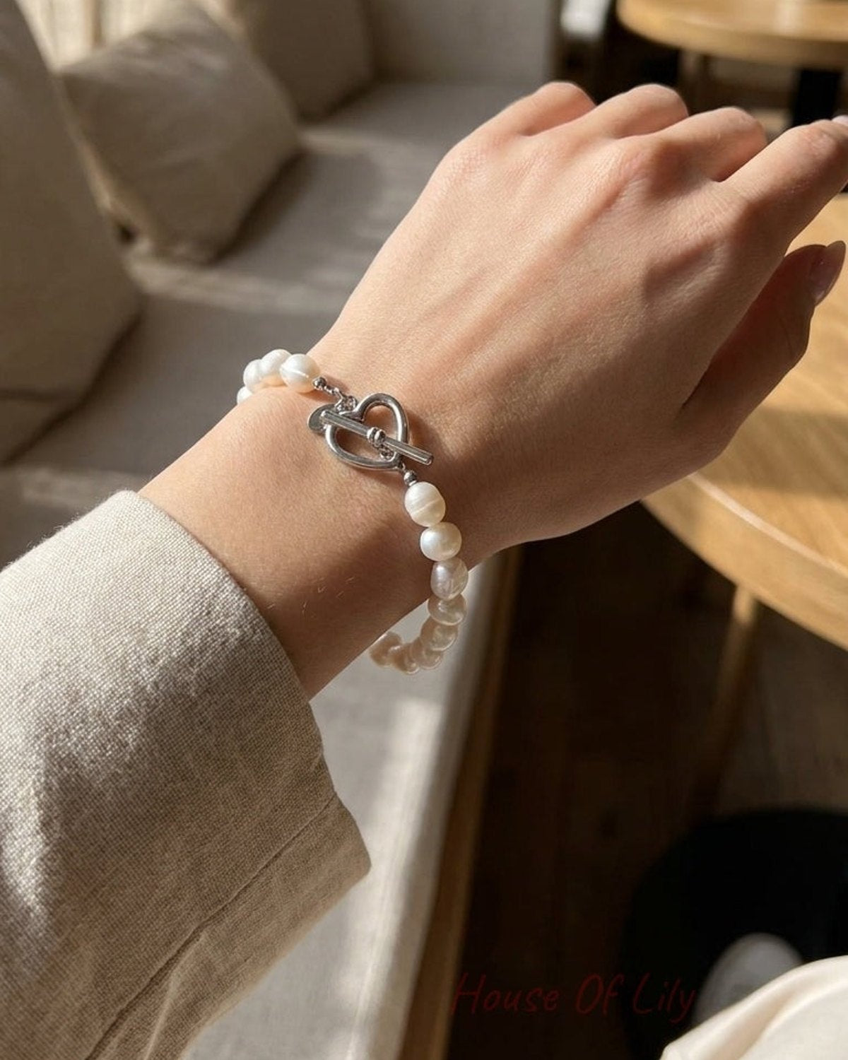 A baroque pearl bracelet with a silver heart toggle clasp on a woman’s wrist.