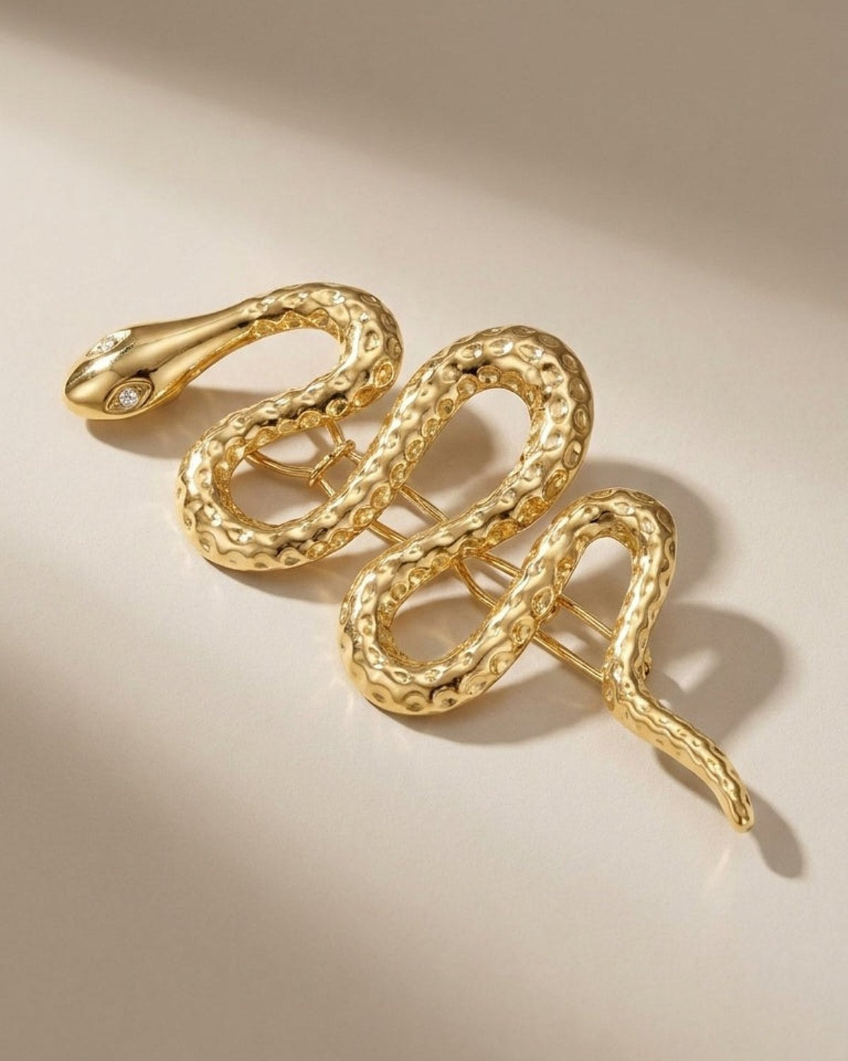 Gold snake brooch with a textured body and crystal eyes, displayed on a light surface.