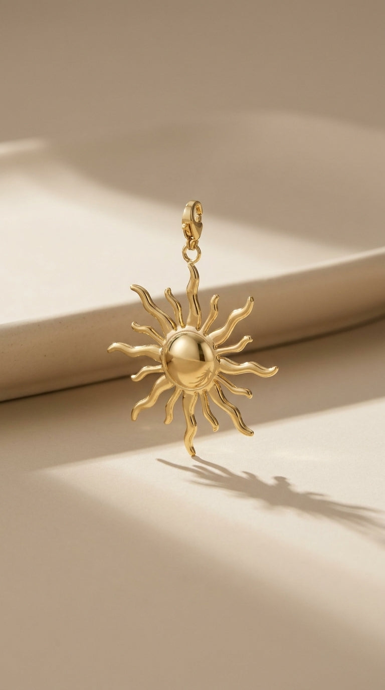 Polished gold sun jewelry charm with wavy rays and a lobster clasp.