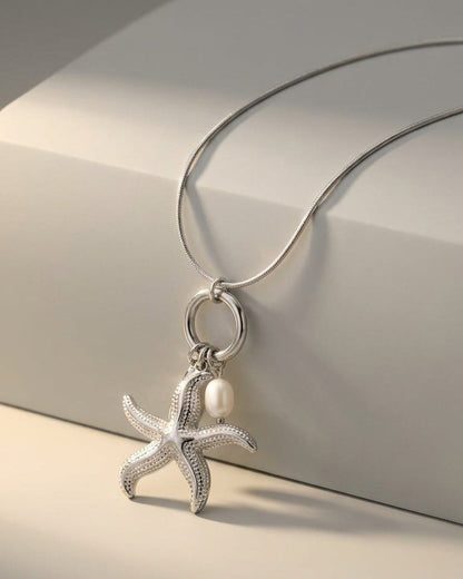 Silver pendant necklace featuring a textured starfish and a small white pearl hanging from a ring bail.