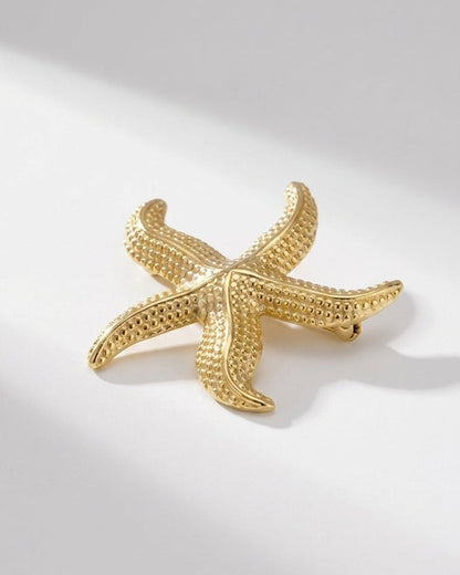 Gold starfish brooch with textured, pebbled details on a white background.