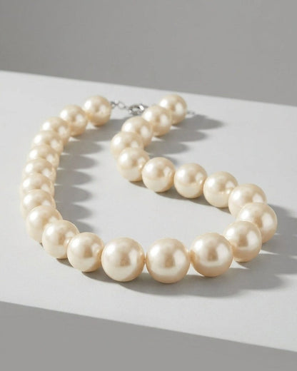 A chunky pearl necklace with large, cream-colored beads resting on a light gray surface.