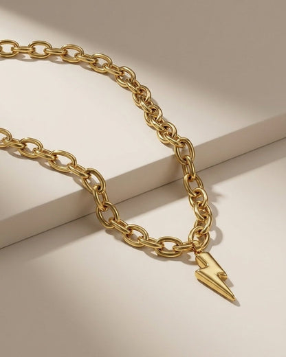 Gold chain necklace with a chunky link design and a lightning bolt pendant resting on a neutral surface.