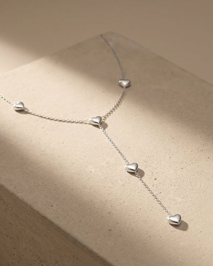 Silver Y-necklace with small puffy heart charms on a fine chain, showcasing a sleek, minimalist style.