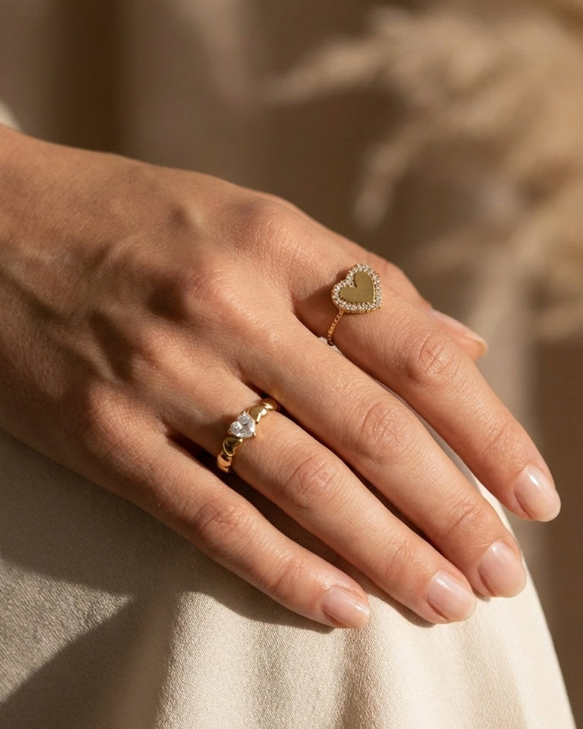 Gold rings on a hand: one features a zircon-studded heart frame, the other a heart-shaped stone.