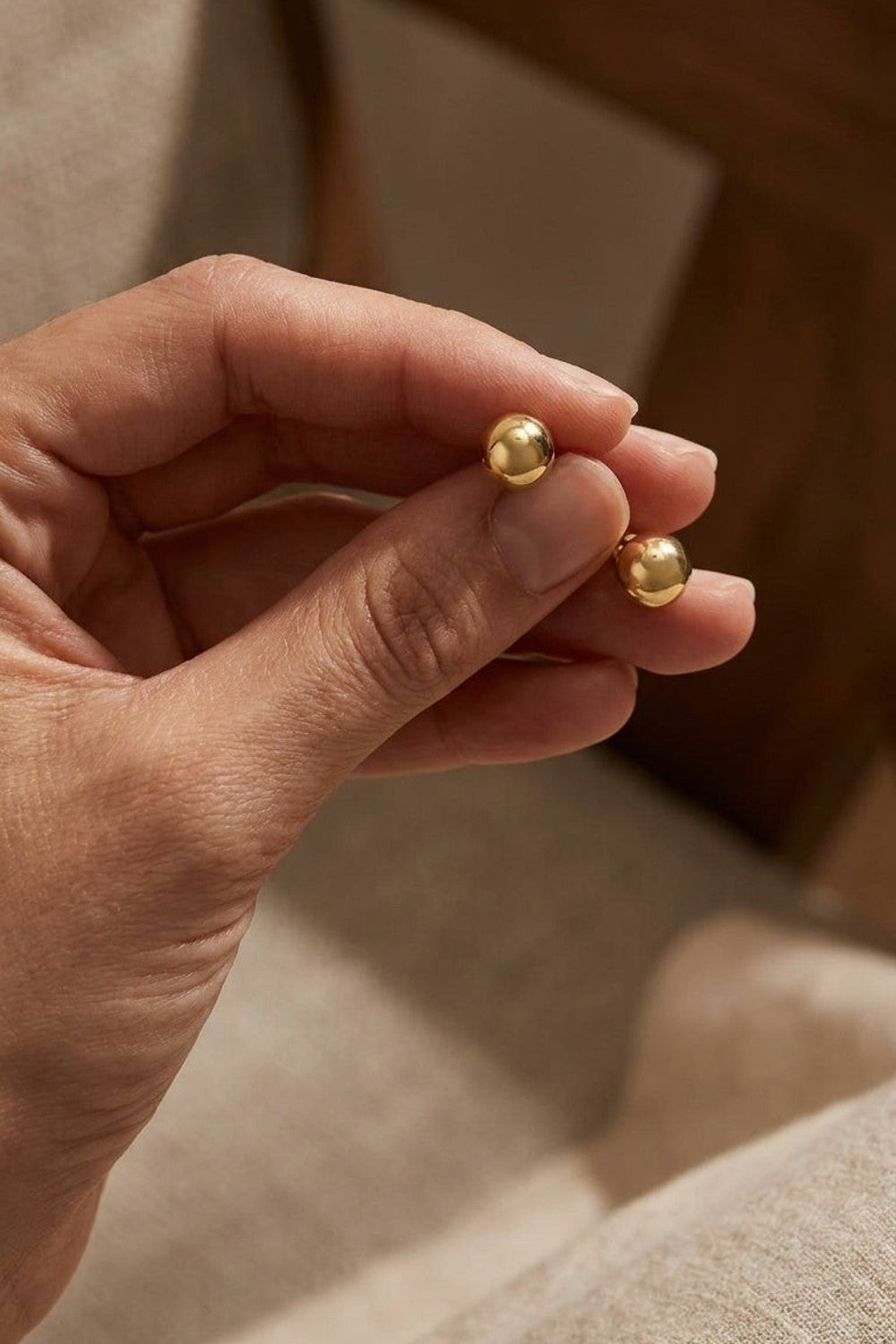 Chic Steel Geometric Studs: two polished gold-tone spherical stud earrings held between fingers.