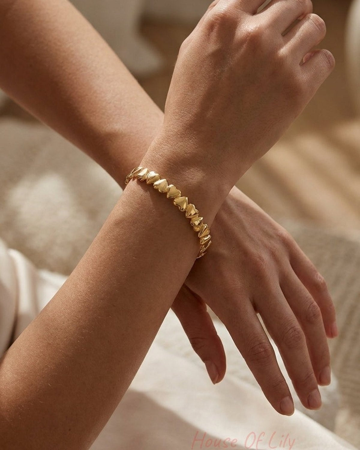 A gold-toned cuff bracelet made of connected small hearts worn on a person's wrist.