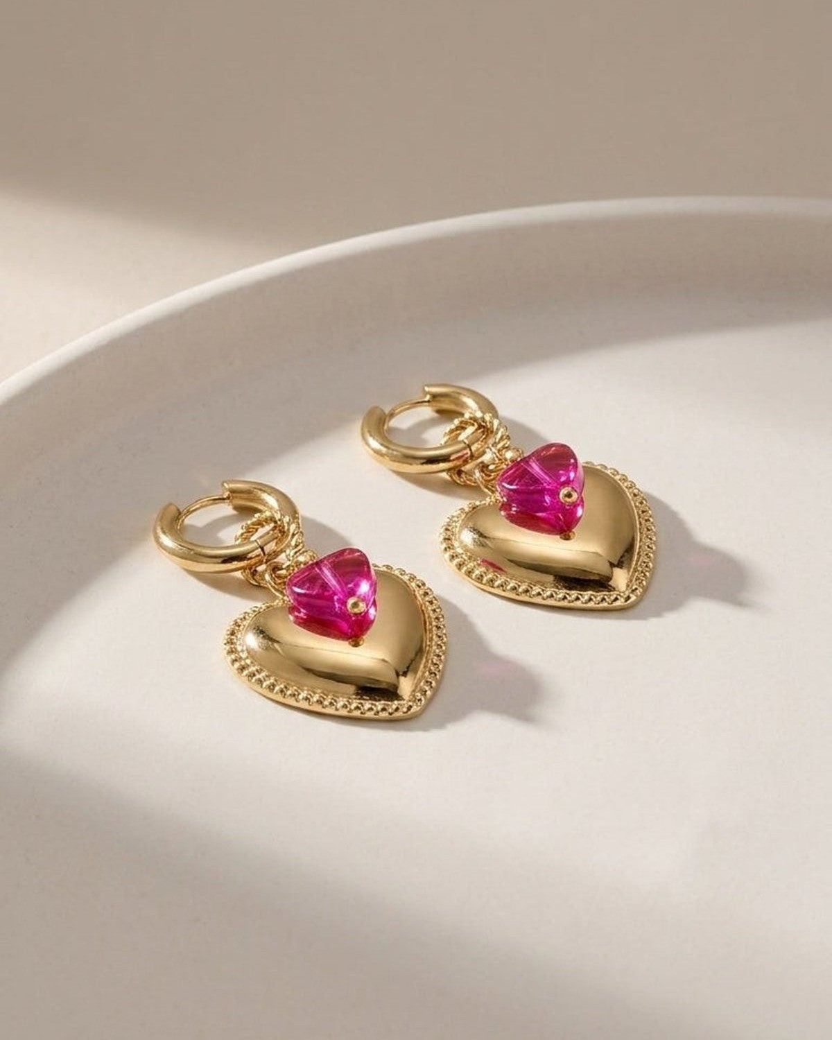 Gold hoop earrings with beaded-edge heart pendants topped with small faceted pink crystal hearts.