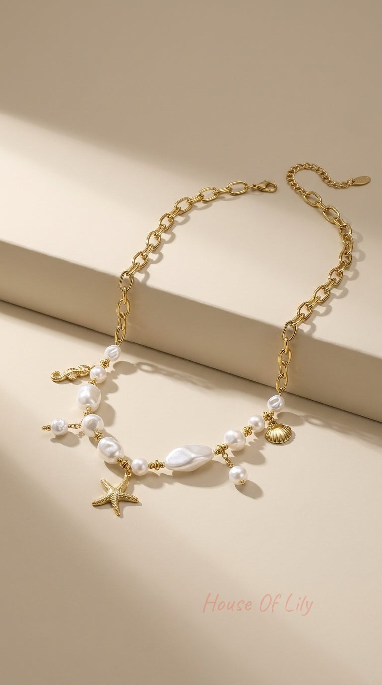 Gold chain necklace featuring baroque pearl beads and dangling starfish, seashell, and seahorse charms.