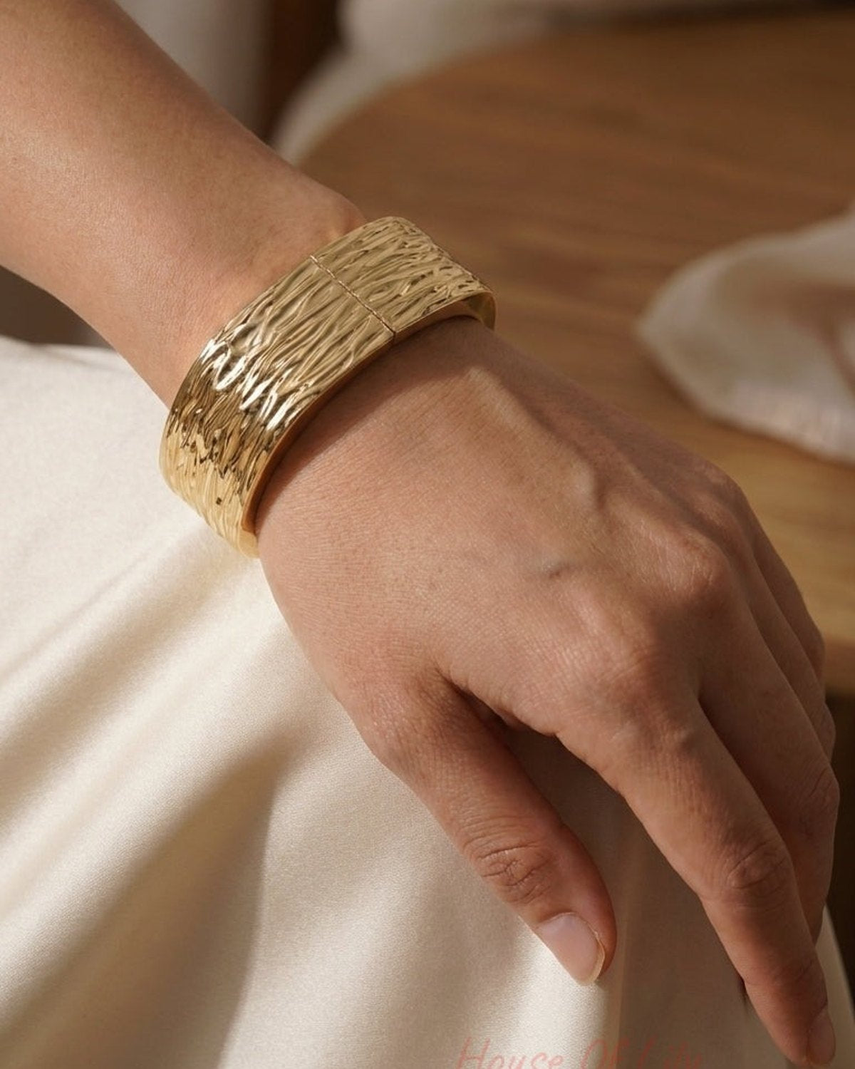 A wide, textured gold-tone metal cuff bracelet is worn on a wrist.