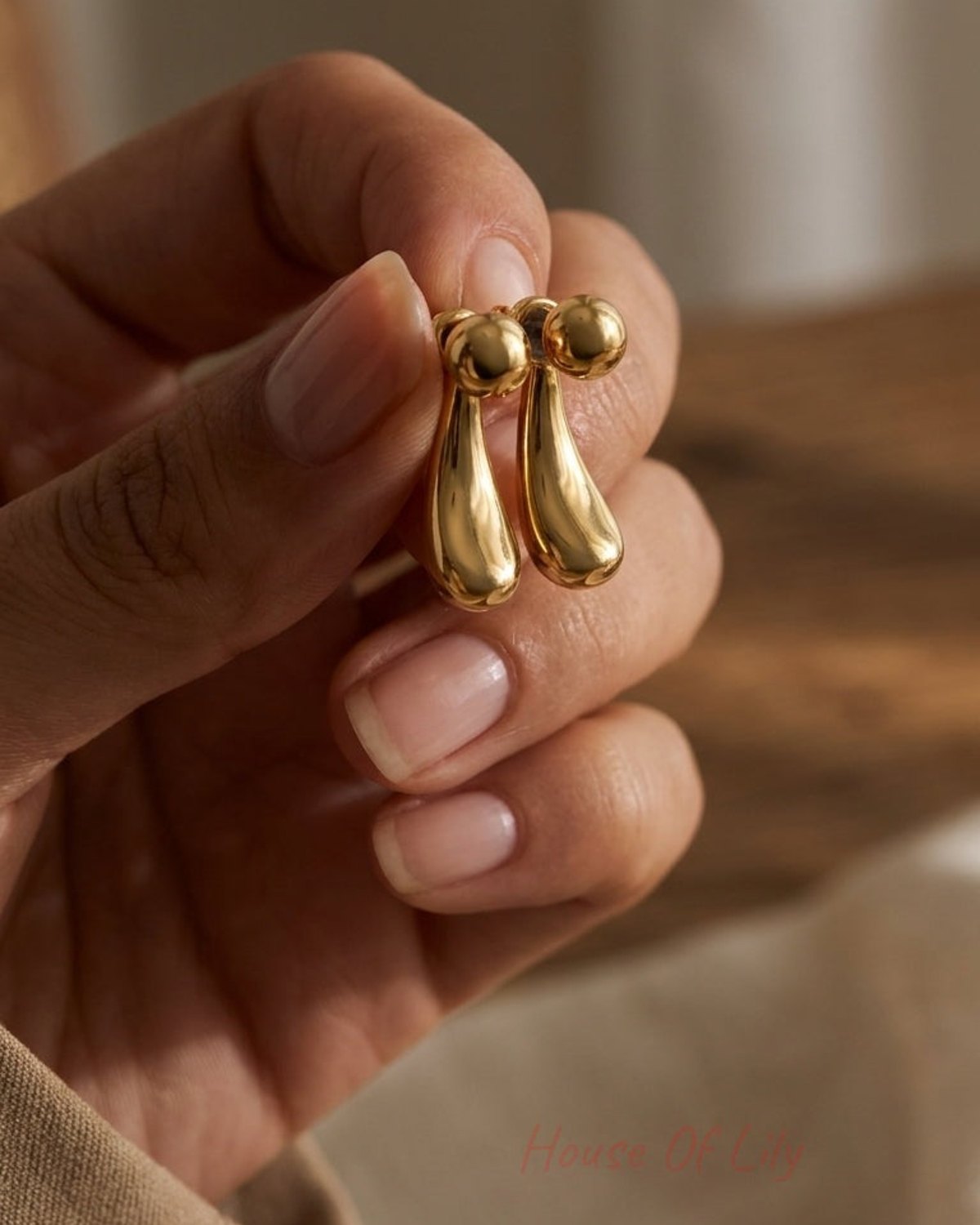 A hand holds two polished gold-tone teardrop-shaped stud earrings.