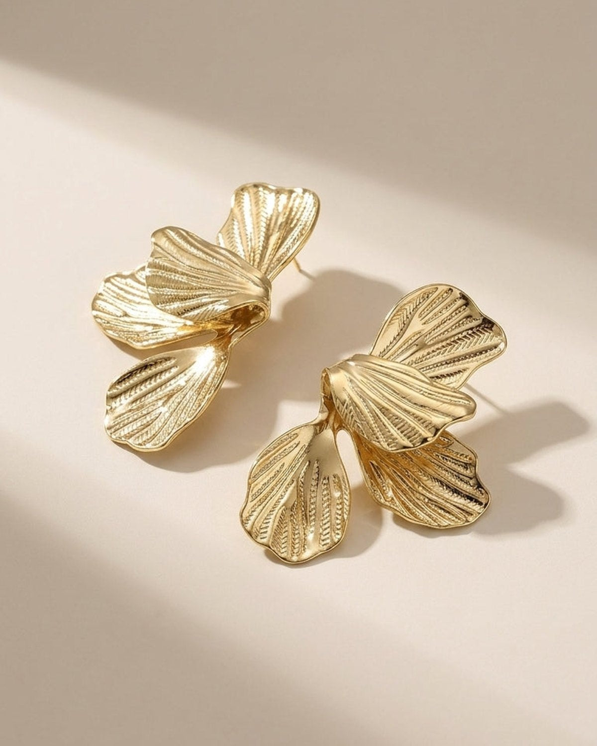 Flower Drop Earrings made of gold metal with a textured petal design on a neutral surface.