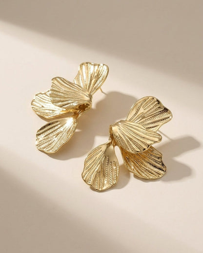 Flower Drop Earrings made of gold metal with a textured petal design on a neutral surface.